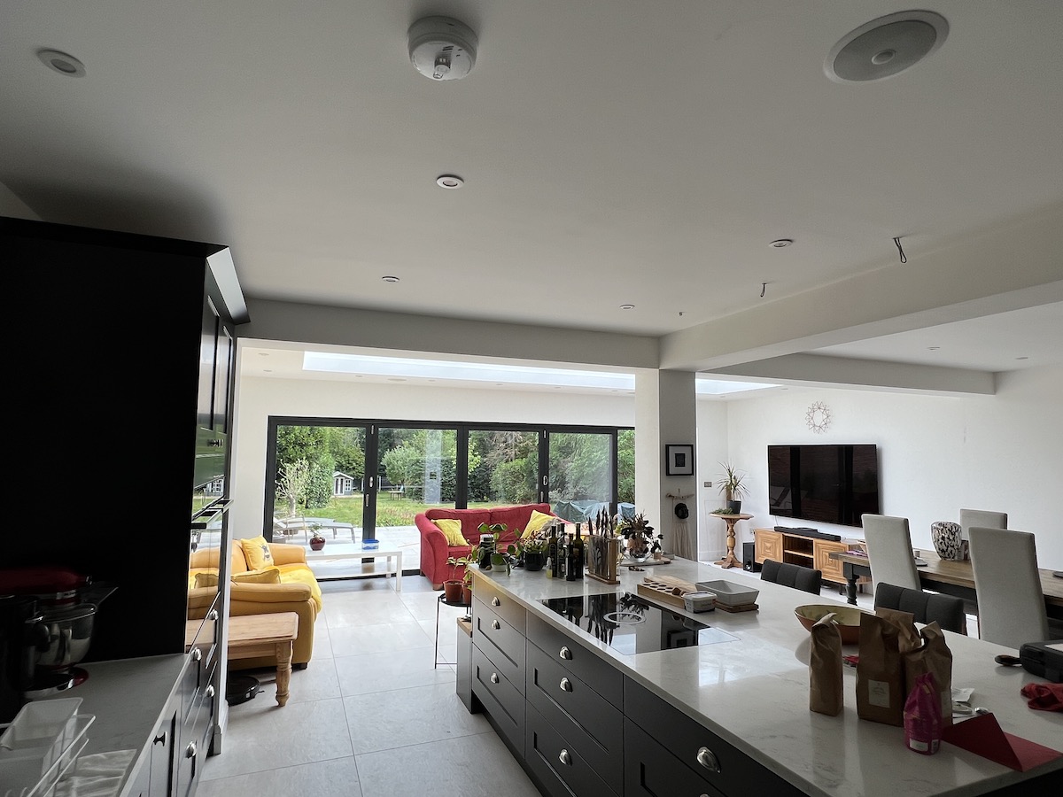 Open-plan kitchen-diner orangery extension in Surrey — central island beneath roof lantern with bifold doors to garden